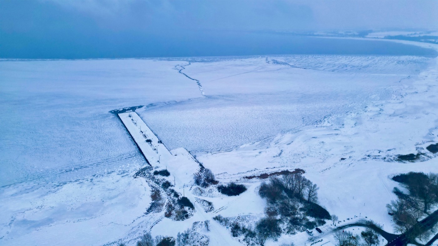 Winterliche Luftaufnahme: die Wiek ist zugefroren, Anleger und Ufer liegen unter einer geschlossenen Schnee- und Eisdecke.